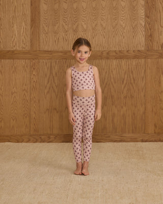 Play by Rylee & Cru Swift Sports Bra - Blush Fleur Play by Rylee & Cru Basic Legging - Blush Fleur Young girl wearing a matching top and pants set with a floral pattern against a wooden wall.