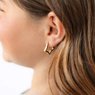 Pip Pop Post Star Hoop
Close-up of a person wearing a gold hoop earring with a blurred background