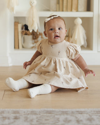 Quincy Mae Darla Dress - Magic
Baby in a beige dress sitting on a wooden floor with a neutral background
