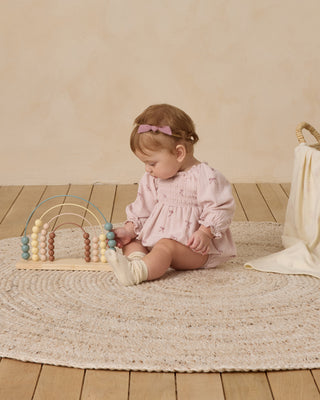 Quincy Mae Eden Romper - Bows
Child playing with a wooden toy on a wooden floor