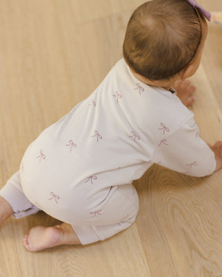 Quincy Mae Relaxed Fleece Jumpsuit - Bows
Baby in light-colored outfit with bow patterns on a wooden floor