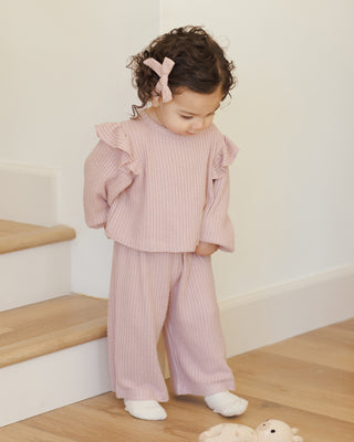 Quincy Mae Ruffle Cozy Set - Rose Child wearing a pink ribbed outfit standing on a wooden floor with a white wall background