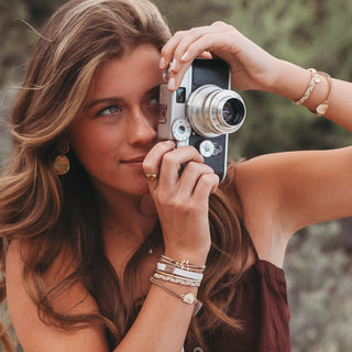 K'lani "Rise" Cream and Tan With Gold and Sun Hair Tie Bracelets
Woman holding a vintage camera with a blurred natural background