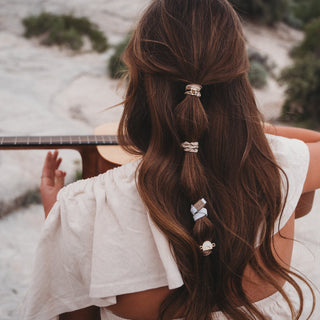 K'lani "Rise" Cream and Tan With Gold and Sun Hair Tie Bracelets
Person with long brown hair in a ponytail with decorative hair ties, sitting outdoors.