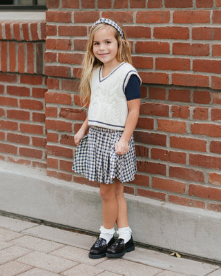 Rylee & Cru Pleated Mini Skirt - Navy Check
Young girl in a checkered dress and sweater standing against a brick wall.