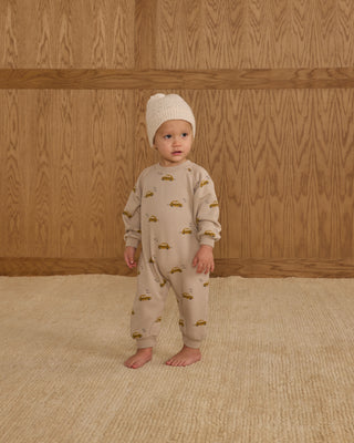 Rylee & Cru Raglan Jumpsuit - Taxi
Baby wearing a beige onesie with car prints and a matching hat, standing against a wooden paneled wall.