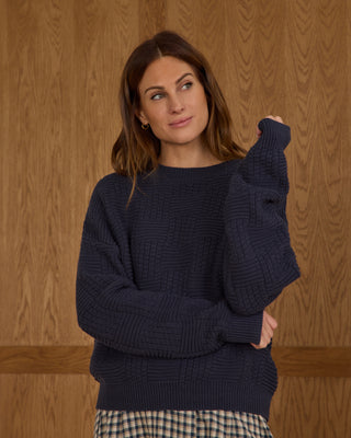 Rylee & Cru Womens Carolina Sweater - Navy Woman wearing a navy blue sweater against a wooden background