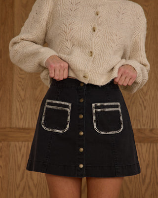 Rylee & Cru Womens Denver Mini Skirt - Washed Black
Person wearing a beige knitted sweater and black skirt with white stitching on a wooden background