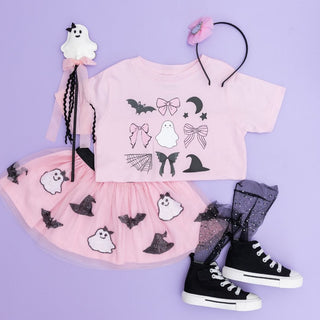 Sweet Wink Spooky Coquette Halloween Short Sleeve T-Shirt - Ballet Pink t-shirt with Halloween-themed graphics, pink skirt with ghost pattern, black shoes, and accessories on a purple background.