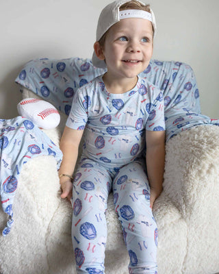Lev Baby Pajama Set - Home Run
Child wearing a patterned onesie sitting on a white couch with pillows.