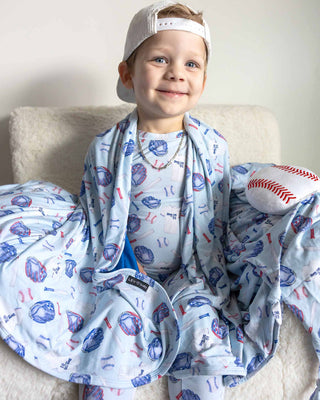 Lev Baby Pajama Set - Home Run
Child wrapped in a baseball-themed blanket with a baseball and cap on a light background