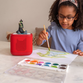 Tonies Character - Wicked
Child painting with watercolors next to a red cylindrical object on a table.