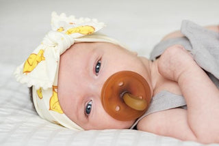 Baby Bling Chicks ivory pom-trimmed knot headband on a baby, featuring soft fabric and decorative pom details.